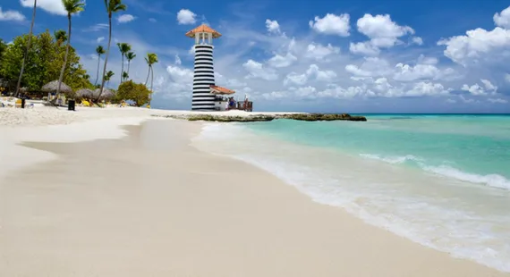 Playa caribeña de arena blanca con palmeras y un faro a rayas, perfecta para vacaciones de verano y turismo