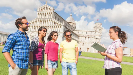 Un grupo de turistas escuchando a su guía frente al Baptisterio y la Torre Inclinada de Pisa en Italia. Tours guiados y viajes a Europa