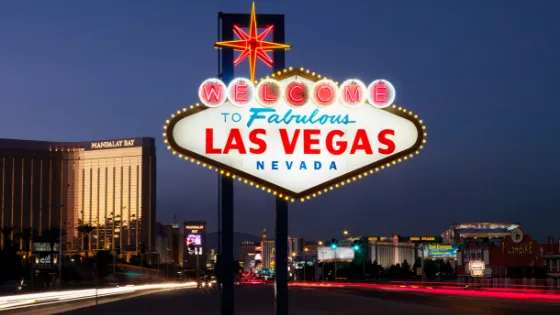 El icónico letrero "Welcome to Fabulous Las Vegas" iluminado de noche, con el Mandalay Bay y otros hoteles al fondo. Viajes a Las Vegas, Nevada y turismo de ocio