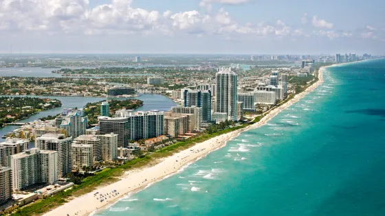 Vista aérea de Miami Beach con playa, rascacielos frente al mar y canales urbanos. Imagen ideal para ilustrar destinos costeros y ciudades con desarrollo turístico